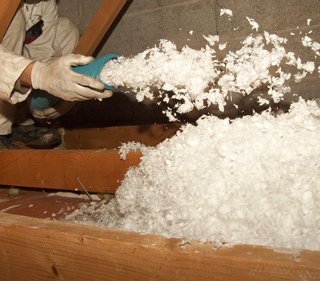 Ouvrier en tenue de protection insufflant de l'isolant soufflé blanc (cellulose ou ouate) dans les solives d'un grenier.