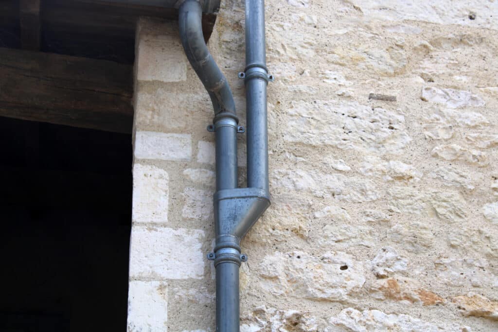Gouttière en zinc gris et cuvette de branchement sur la façade de la maison en pierre
