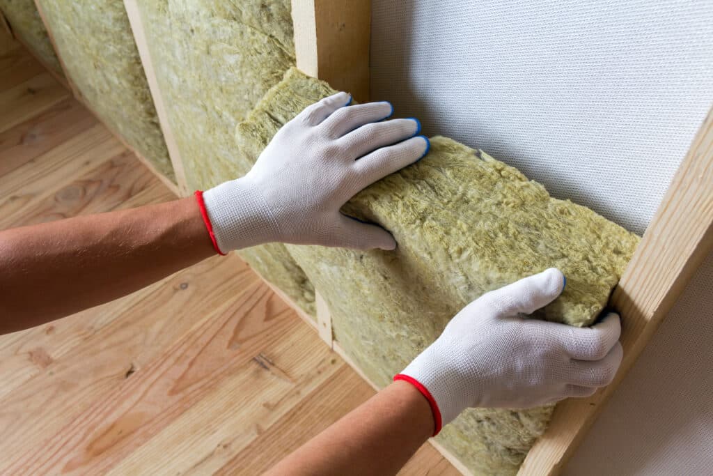 Close-up of worker hands in white gloves insulating rock wool in