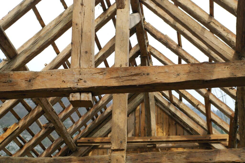 Charpente en bois brut d'une structure en construction ou rénovation, gros plan sur les poutres et poteaux sous un ciel blanc.
