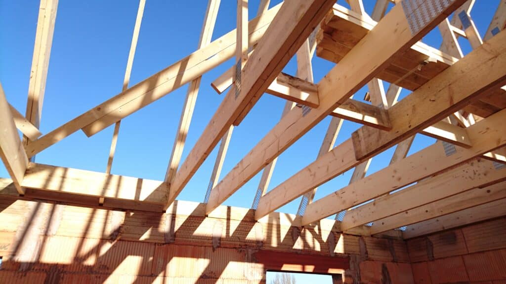 Charpente en bois neuve d'une maison en construction avec murs en briques poreuses visibles en dessous, sous un ciel bleu clair.