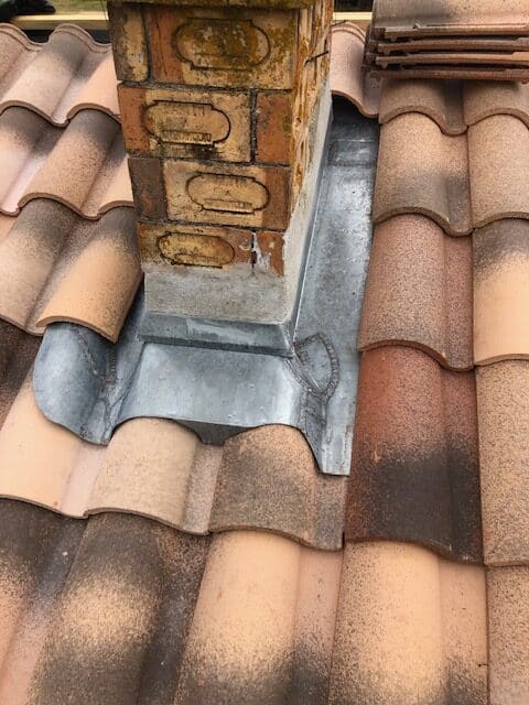 Étanchéité de cheminée : abergement en zinc et tuiles Abergement d'étanchéité en zinc sur une cheminée en brique et toiture de tuiles romanes.