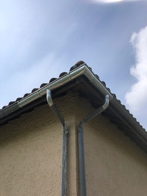 Gouttières métalliques et descentes d'eaux pluviales Gouttières métalliques et descentes d'eaux pluviales sur le coin d'une maison avec toiture en tuiles.