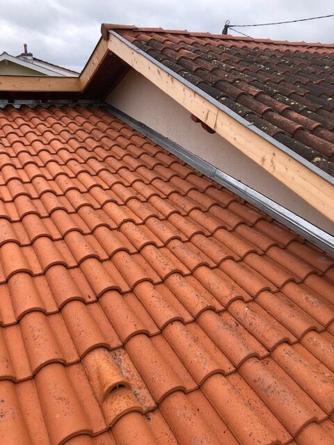 Rénovation de Toiture : Tuiles Romanes et Zinguerie Toiture en tuiles romanes orange avec solin d'étanchéité et pignon en bois sous un ciel nuageux.